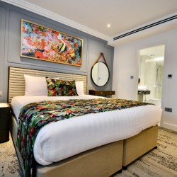 bedroom with king sizee bed, colourful art works, mirror and side table,