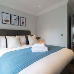 king bed with cushions and towels, view to hallway, Barons Court Apartments, Hammersmith, London W6